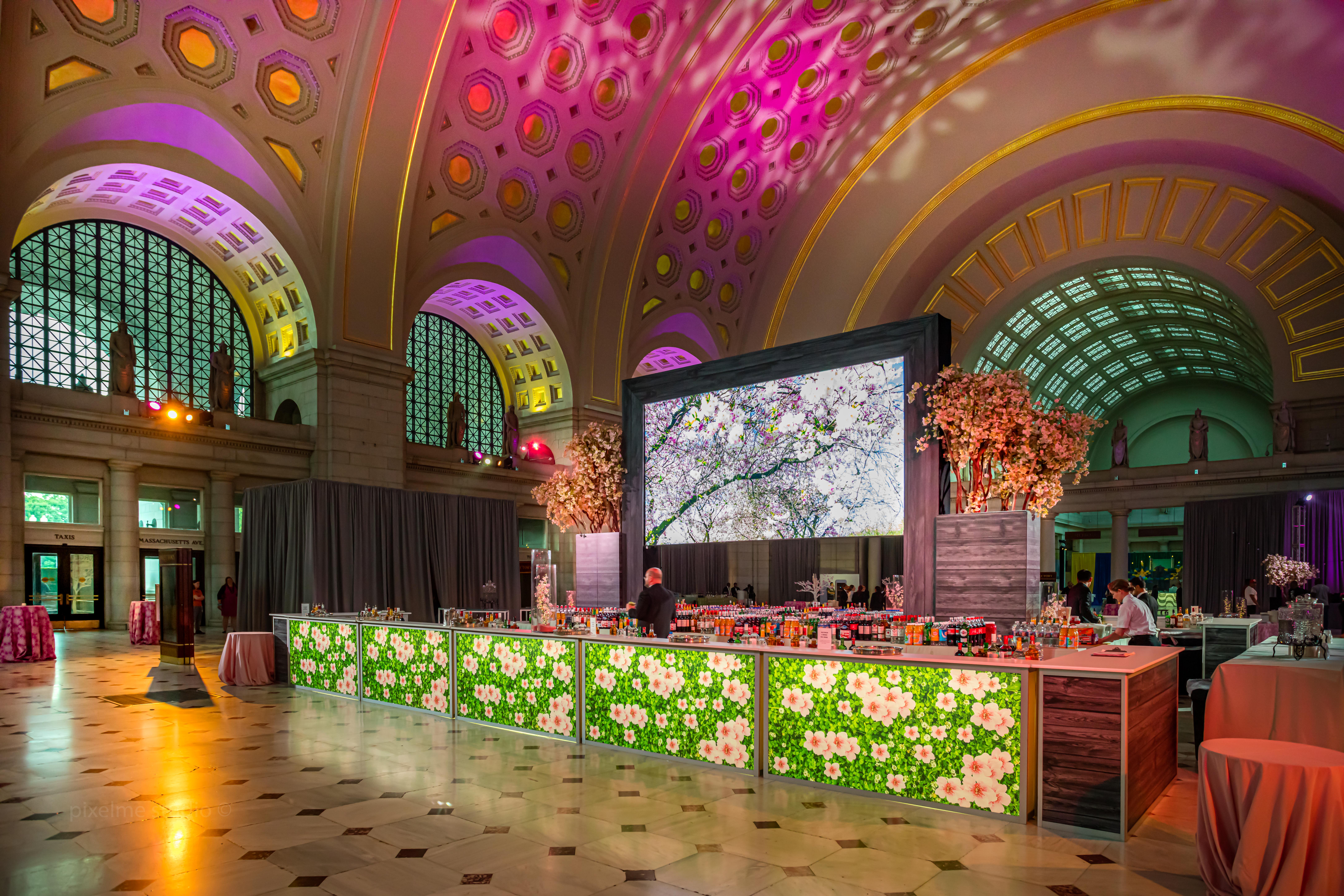 Corporate Event Cocktail Reception in Main Hall featuring a Custom Cherry Blossom Bar, Cherry Blossom Trees, Cocktail Tables, and Pink Up-Lighting.