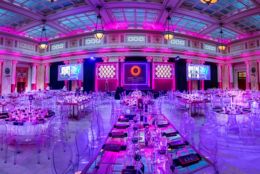 Corporate Event in East Hall featuring Standard Rounds and Gold Mirrored Community Tables. Additionally featured is a Stage with Podium and 4 Large Screens.